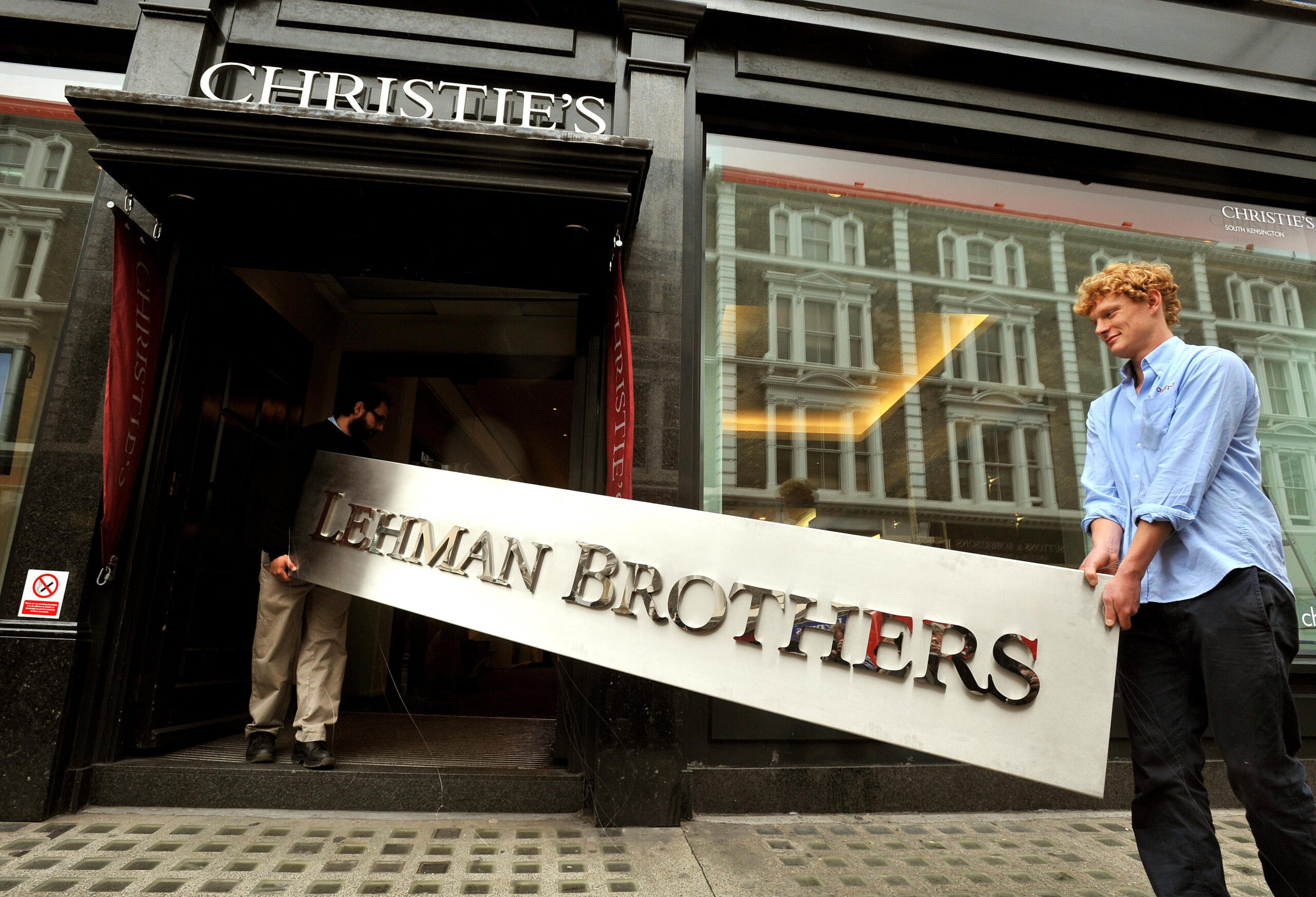 Christie's employees walk into the auction rooms with the main sign from the Lehman Brothers office collection during a photo call at Christie's in west London, before it goes under the hammer on September 29.