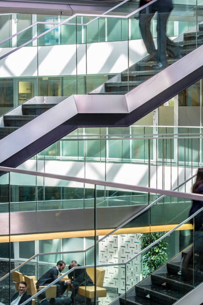 Businesspeople having discussion in office building, people walking though staircase and corridor.